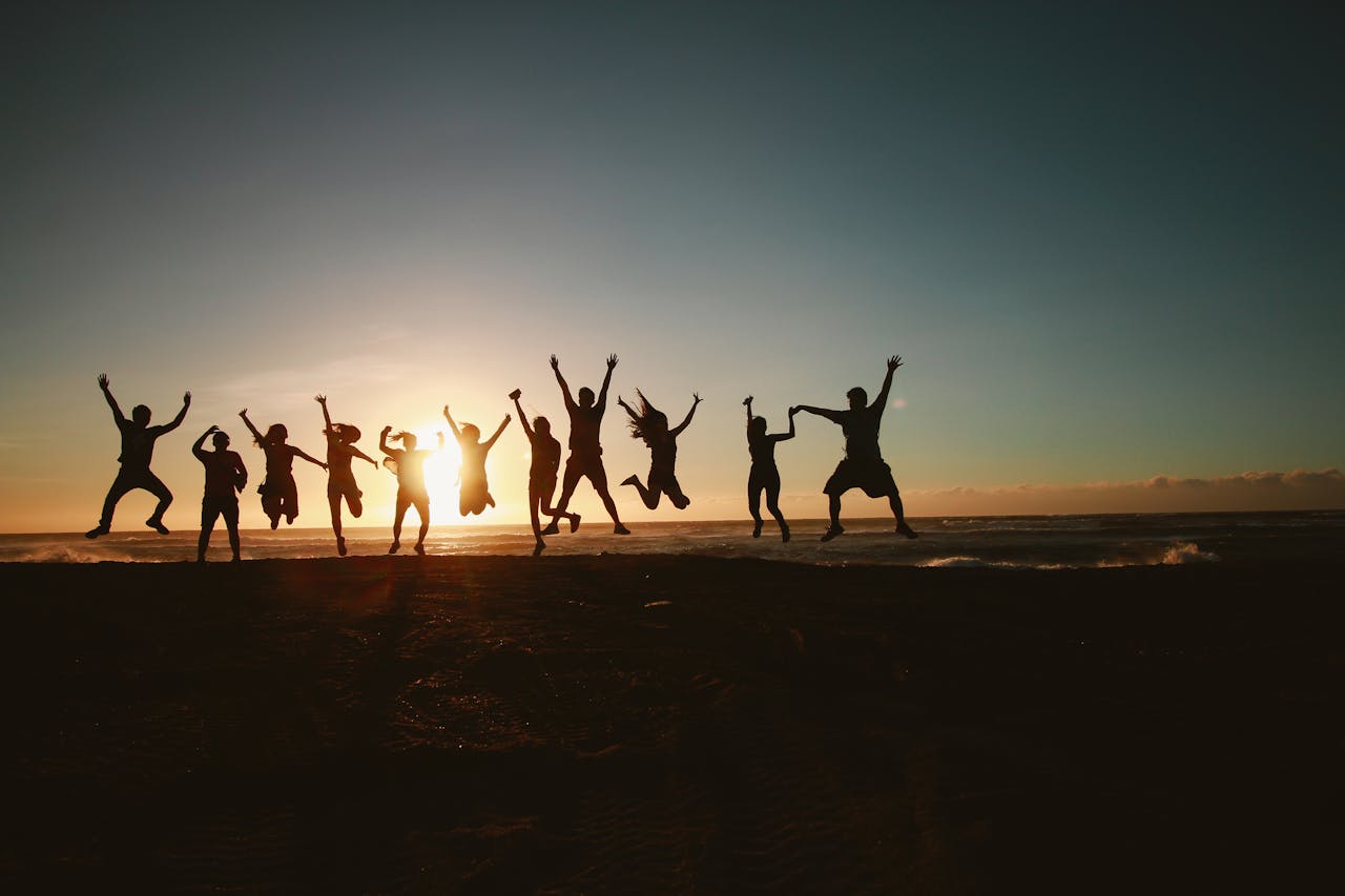 about-img Silhouette of a group of friends jumping on a beach at sunset, expressing joy and freedom.