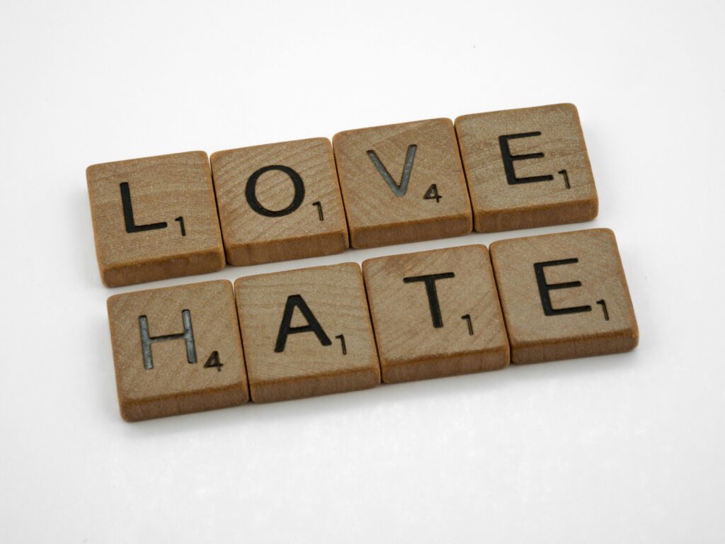 pexels photo 10220429 10220429 Close-up of wooden Scrabble tiles spelling 'Love' and 'Hate' on a white background.