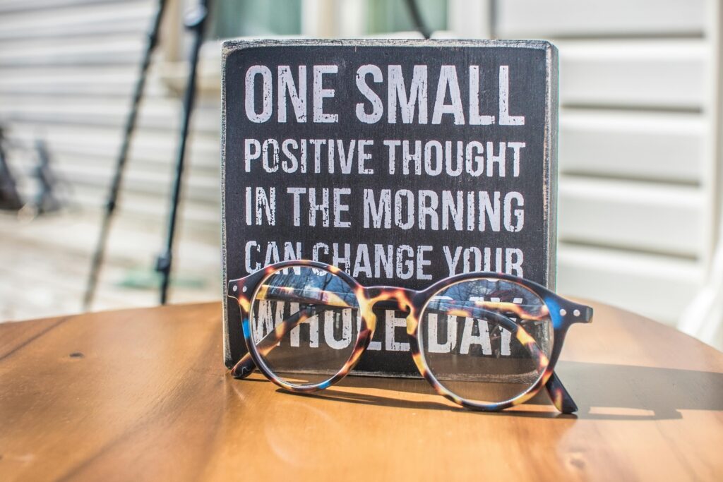 pexels photo 1485657 1485657 Eyeglasses resting on a table in front of a motivational quote sign, emphasizing positivity.