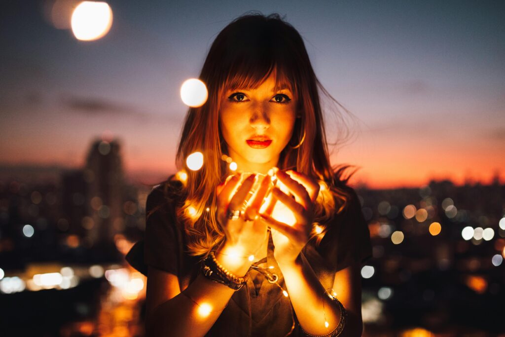 pexels photo 573299 573299 Romantic portrait of a woman holding glowing string lights against a city skyline at dusk.